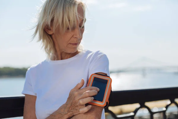 Athletic elderly lady tracking distances with phone in arm band