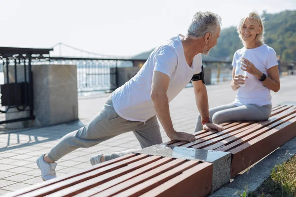 Smiling woman watching her husband do stretching exercises — Stock Photo, Image