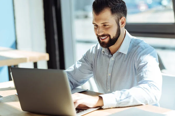 Agradável sorridente homem usando seu laptop no escritório — Fotografia de Stock