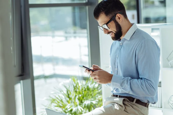 Joyful young man sending text messages at work