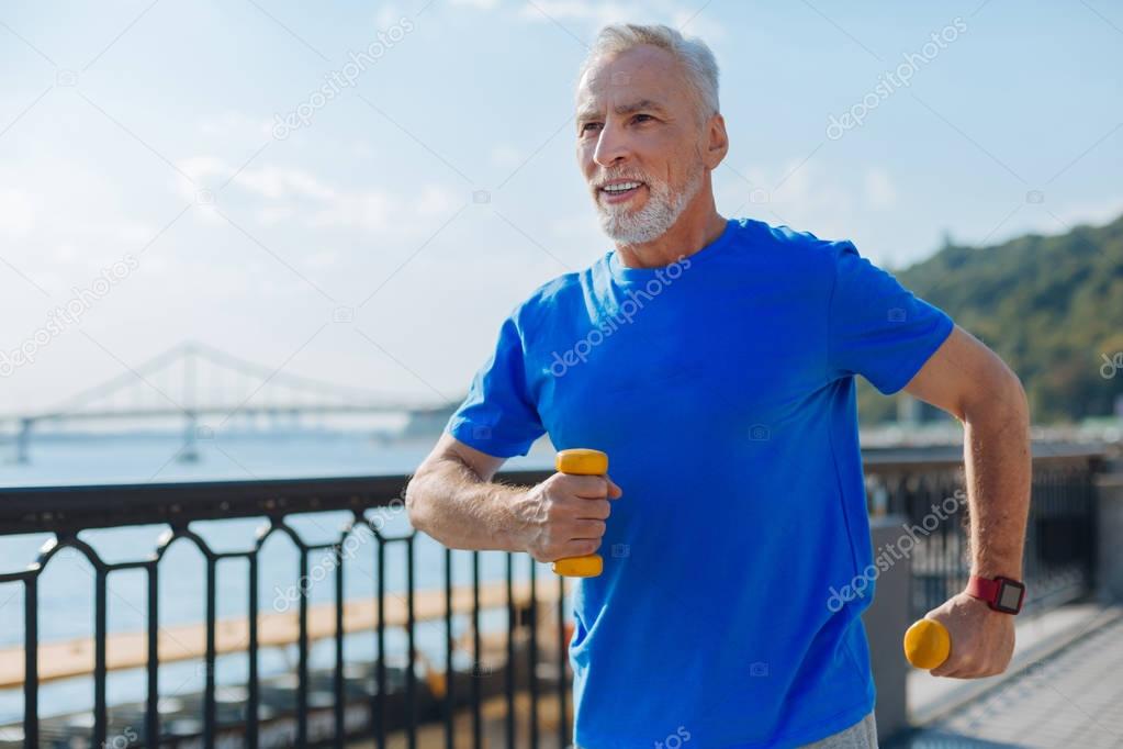 Athletic senior man jogging with dumbbells