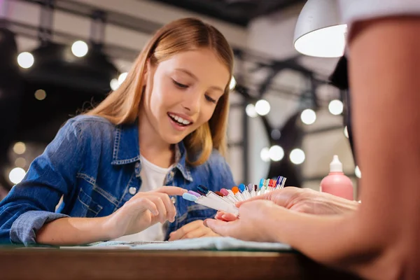 Chica alegre eligiendo su futuro color de uñas de una paleta —  Fotos de Stock