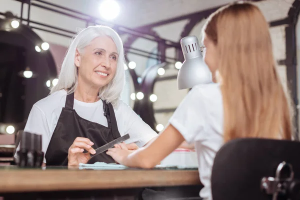 Manicurista sonriente dando forma a las uñas de su cliente adolescente — Foto de Stock