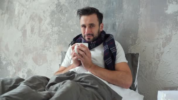 Armer junger Mann trinkt warmen Tee während er sich krank fühlt — Stockvideo