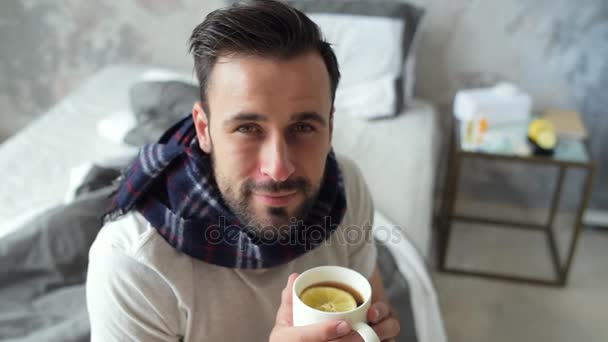 お茶を飲みながらカメラに探している病気の男の笑みを浮かべてください。 — ストック動画