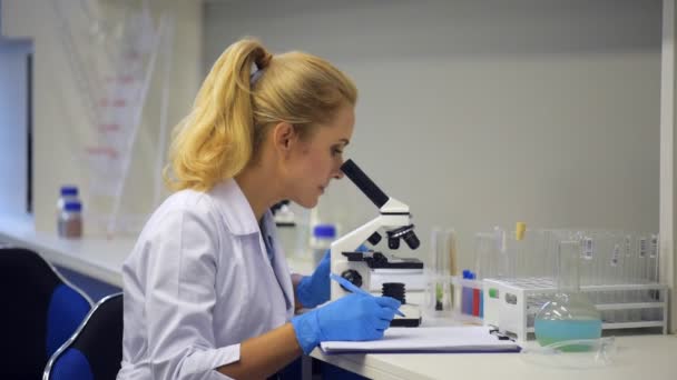 Cheerful researcher looking through microscope and smiling into camera — Stock Video