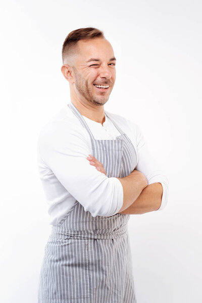 Cheerful man in apron folding arms and winking
