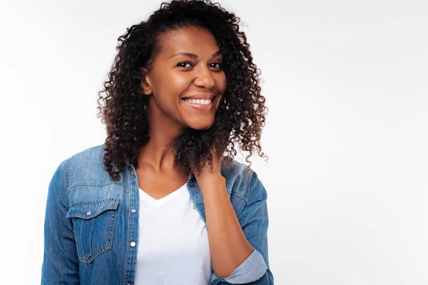Cheerful curly woman holding hand in hair and smiling — Stock Photo, Image