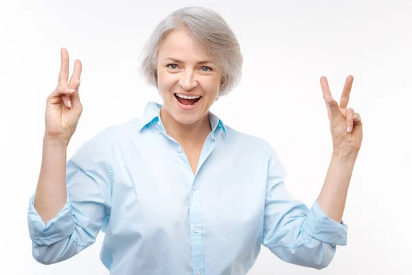 Веселая седовласая женщина с V-знаками обеими руками — стоковое фото