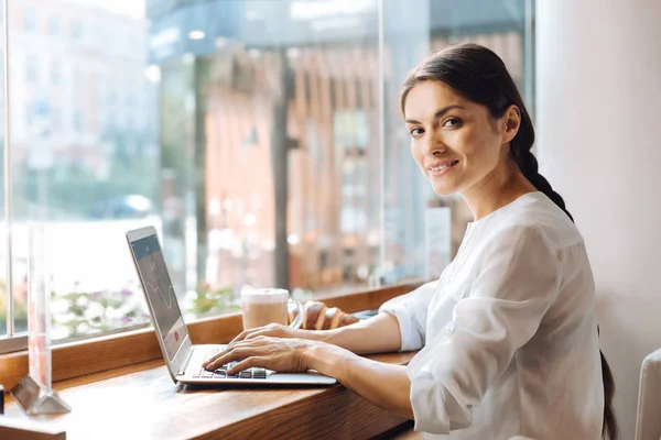 Femme optimiste tapant sur un ordinateur portable dans un café — Photo