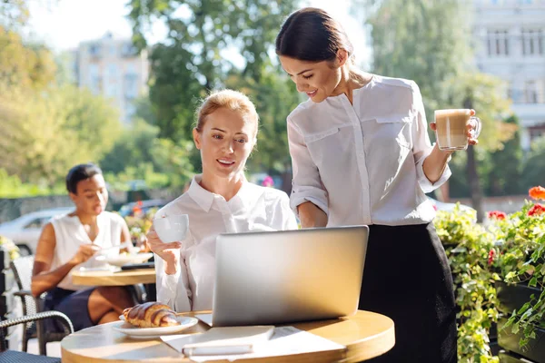 Trevlig kvinna som tittar på hennes kollegor laptop i café — Stockfoto