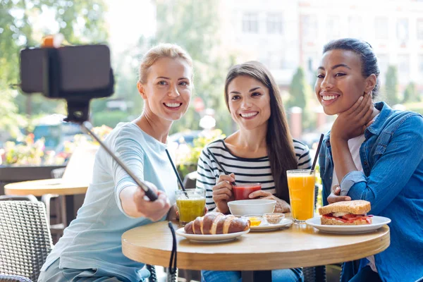 Mulheres encantadoras tomando selfies com monopod no café — Fotografia de Stock