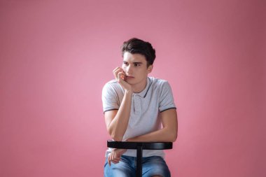 Pembe arka plan üzerinde oturan genç adam bitkin