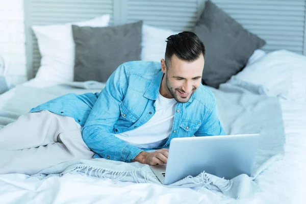 Jovem animado sorrindo enquanto usa laptop — Fotografia de Stock