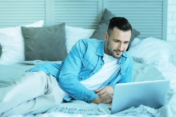 Avslappnad tusenåriga kille i sängen med laptop — Stockfoto