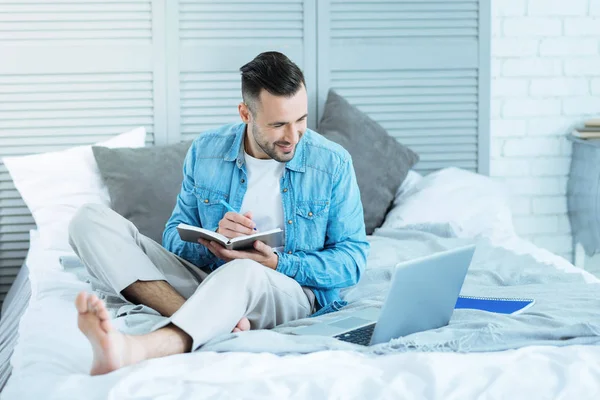 Glad ung herre anteckningar medan du använder laptop — Stockfoto