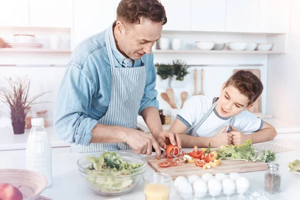 Pequeño hijo viendo a su padre cortar verduras en rodajas — Foto de Stock