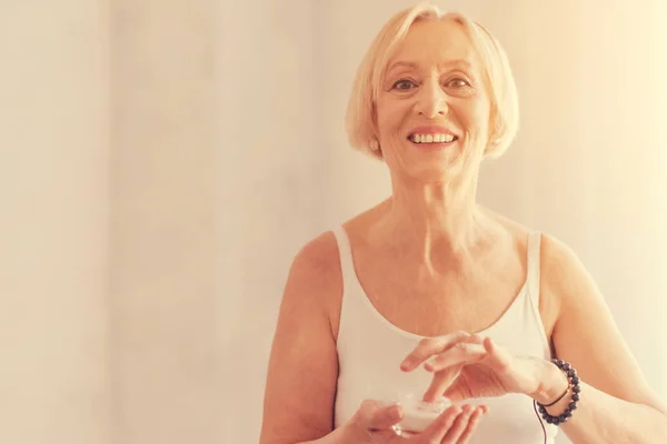 Fröhliche Seniorin, die Anti-Aging-Gesichtscreme aufträgt — Stockfoto