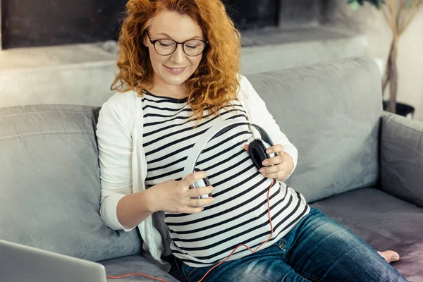 Веселая беременная женщина держит наушники в руках — стоковое фото
