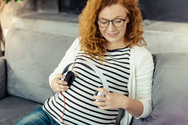 Omtenksom, gravid kvinne med øretelefoner – stockfoto