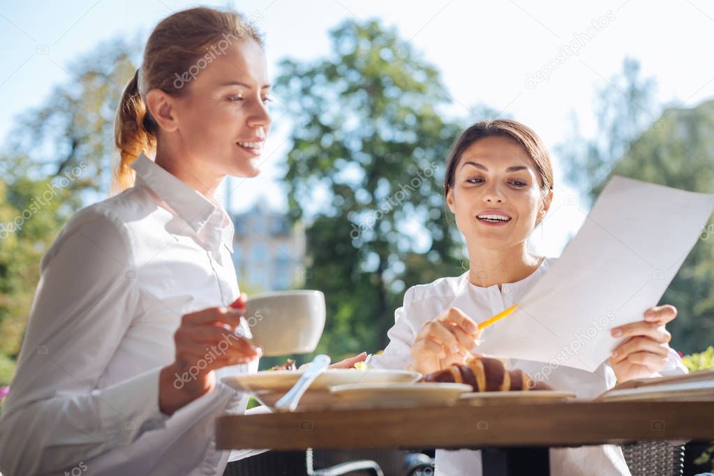 Pleasant woman explaining data on printouts to colleague in cafe