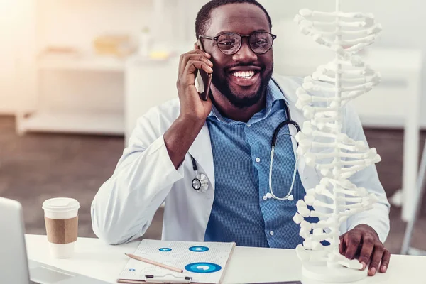 Profesional médico joven de mente positiva hablando por teléfono y sonriendo — Foto de Stock