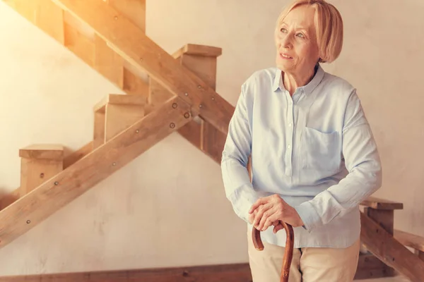 Pleasant thoughtful aged woman standing with a walking stick — Stock Photo, Image