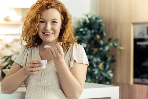Улыбающаяся женщина ест йогурт на кухне — стоковое фото