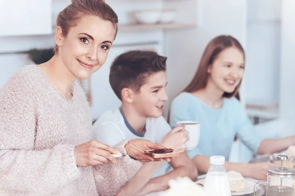 Bela mãe sorrindo enquanto toma café da manhã com a família — Fotografia de Stock