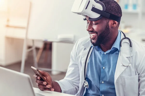 Médico afro-americano relaxado em óculos de realidade virtual usando smartphone — Fotografia de Stock