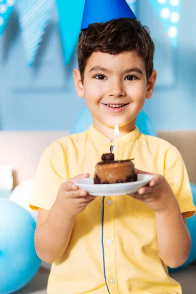 Garoto sorridente em um chapéu de festa posando com bolo de aniversário — Fotografia de Stock