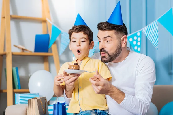Веселые сын и отец задувают свечи на торте на день рождения — стоковое фото