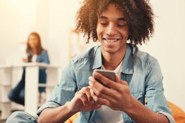 Gülümseyen adam yerde otururken bir akıllı telefon tutarak