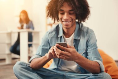 Bir rahat puf sandalyede oturuyor ve bir akıllı telefon tutarak neşeli öğrenci