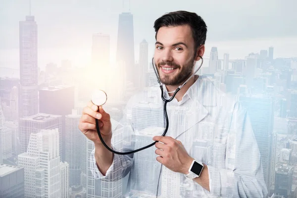 Milý mladý lékař stojící se stetoskopem v pravé ruce — Stock fotografie
