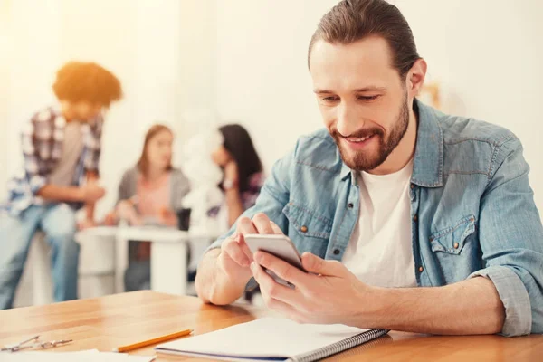 Uomo barbuto sorridente digitando un messaggio sul suo smartphone — Foto Stock