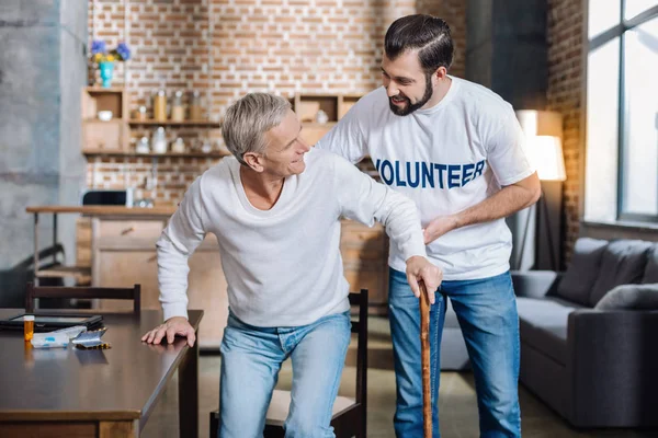 Försiktig uppmärksam volontär att hjälpa en äldre man att stå upp — Stockfoto