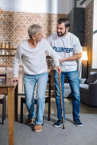 Glada socialarbetare som talar till en pensionär, samtidigt som den hjälper honom att gå — Stockfoto