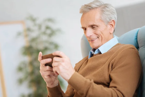 Радостный пожилой мужчина смотрит на смартфон и весело улыбается. — стоковое фото