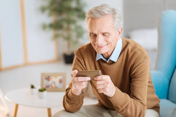 Сияющий пожилой человек смотрит на фотографии со своего смартфона — стоковое фото