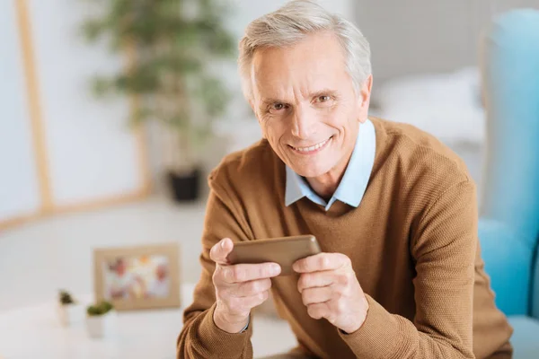 Gioioso vecchio gentiluomo sorridente mentre usa il suo telefono — Foto Stock