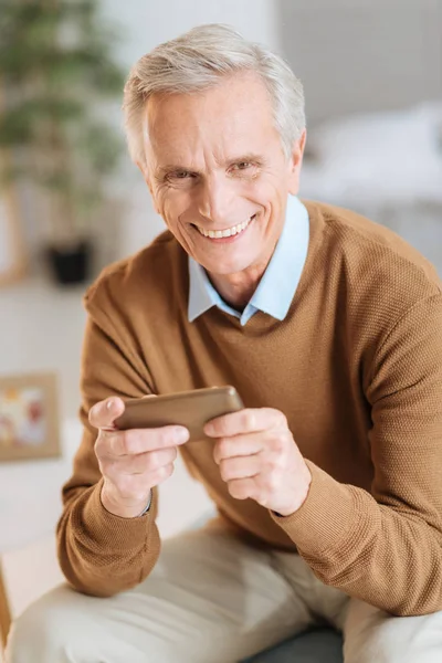 Eccitato uomo anziano ridendo mentre tiene smartphone — Foto Stock