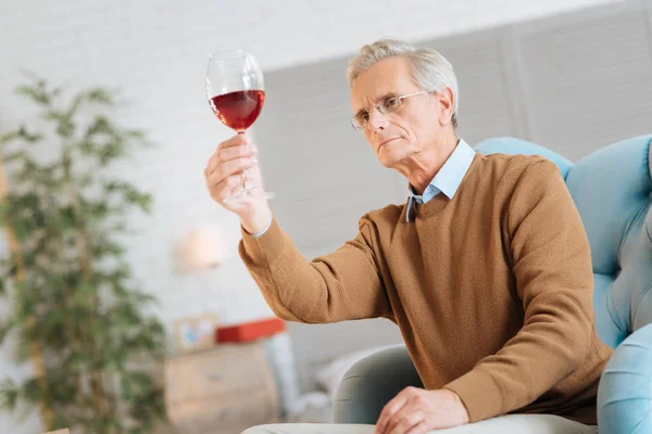 Sábio senhor sênior olhando para o vinho tinto atentamente — Fotografia de Stock