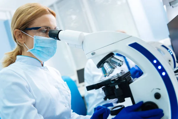 Joven investigador rubio serio mirando en el microscopio —  Fotos de Stock