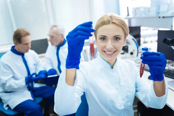 Χαμογελώντας επιστήμονας κρατώντας δοκιμαστικούς σωλήνες και φορώντας μια ομοιόμορφη — Φωτογραφία Αρχείου