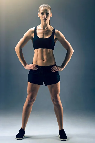 Muscular young sportswoman posing with hands on hips — Stock Photo, Image