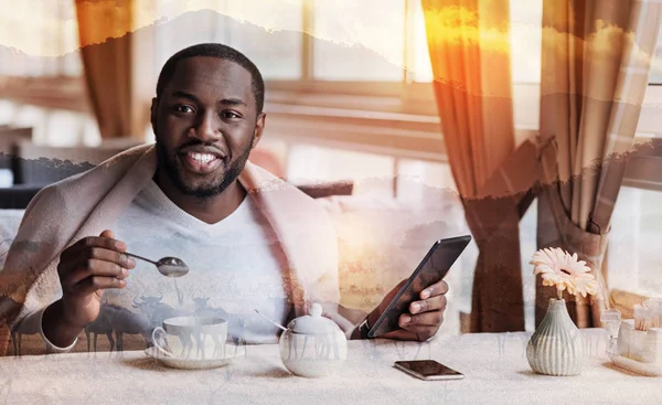 Χαρούμενος νεαρός άνδρας κάθεται σε ένα καφέ με τις σύγχρονες συσκευές και πίνοντας τσάι — Φωτογραφία Αρχείου
