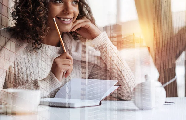 Jovencita sonriente alegre tomando notas mientras está sentada a la mesa — Foto de Stock