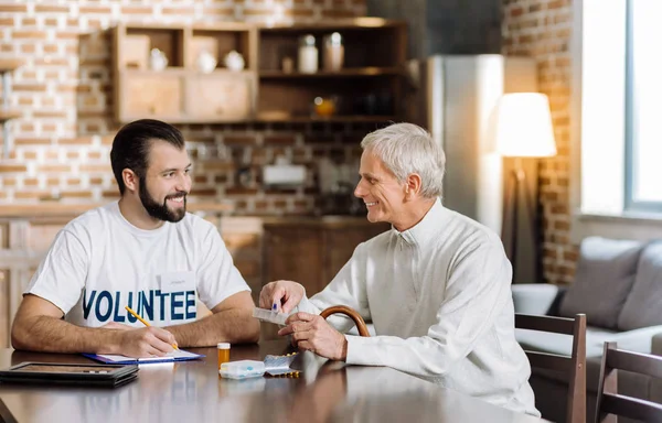 Счастливый старик обсуждает свое лечение с позитивным молодым добровольцем — стоковое фото