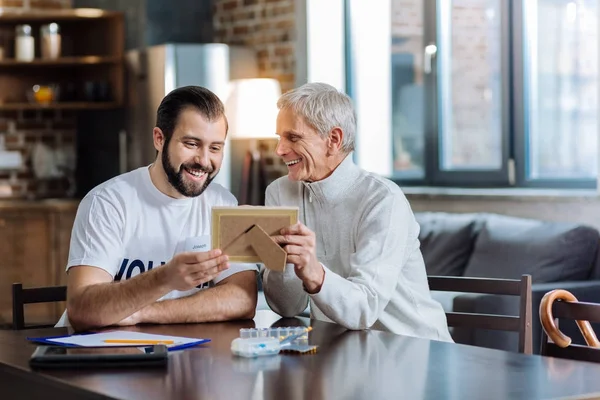 Joven alegre mirando atentamente la vieja foto de un pensionista — Foto de Stock